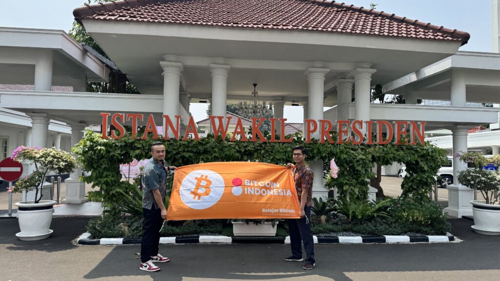Dos personas posan delante un edificio y muestran una bandera naranja