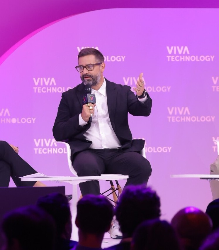 Pascal Gauthier, CEO de Ledger habla en conferencia Viva Technology, fondo rosa con logo, gesto explicativo.