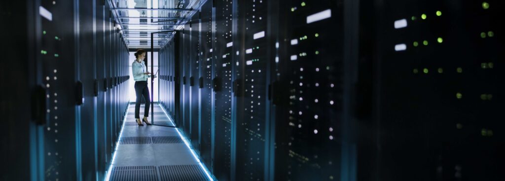 Mujer ingeniera en pasillo de centro de datos iluminado con servidores y luces LED azules

